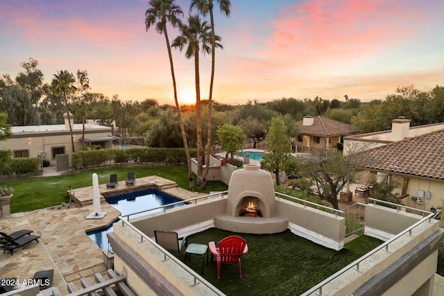 pool at dusk featuring a patio, exterior fireplace, and a lawn