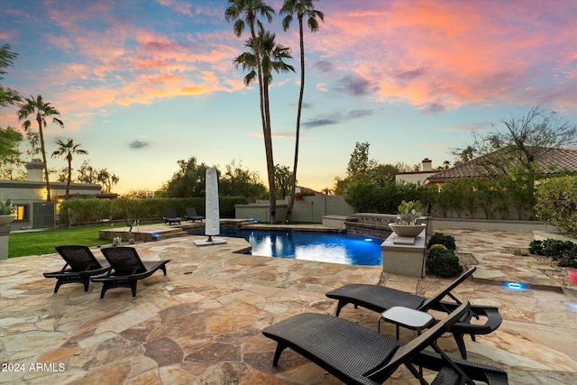 pool at dusk with pool water feature, a patio, and a hot tub