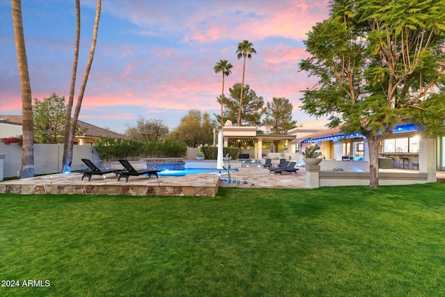 pool at dusk with a patio area and a lawn