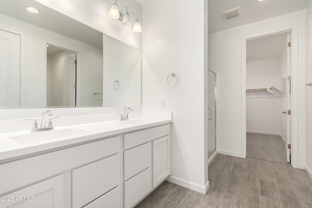 full bathroom featuring a shower stall, a spacious closet, visible vents, and a sink