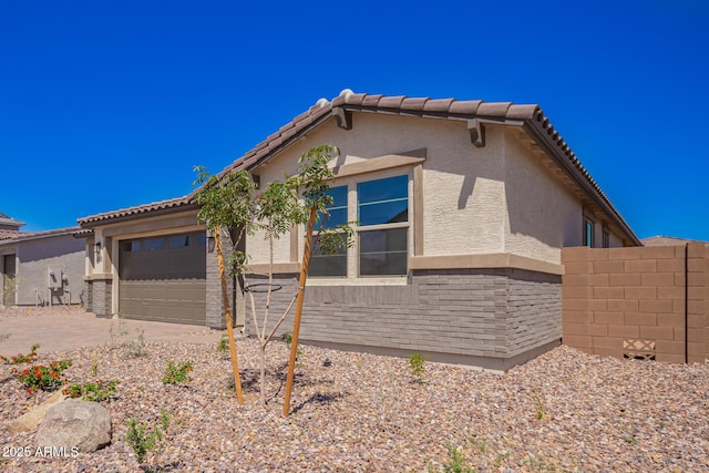 view of side of property featuring concrete driveway, stucco siding, a tile roof, and a garage