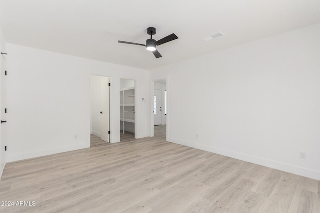 unfurnished bedroom featuring ceiling fan, light hardwood / wood-style floors, a walk in closet, and a closet