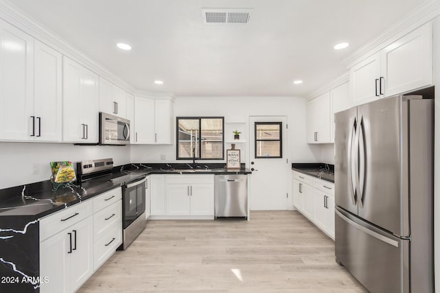 kitchen with appliances with stainless steel finishes, sink, dark stone countertops, light hardwood / wood-style floors, and white cabinetry