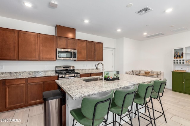 4562 S Park Grove St Unit 101, Gilbert, AZ 85297 - kitchen featuring stainless steel appliances, an island with sink, light stone countertops, a breakfast bar area, and recessed lighting