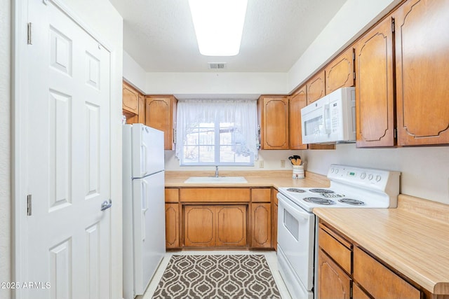 kitchen with light countertops, white appliances, brown cabinetry, and a sink