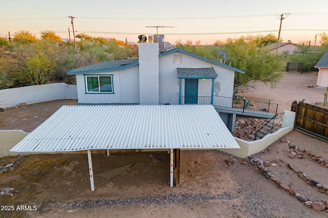 back of house at dusk featuring a chimney, fence, and cooling unit