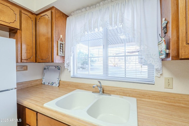 kitchen featuring light countertops, brown cabinetry, a sink, and freestanding refrigerator