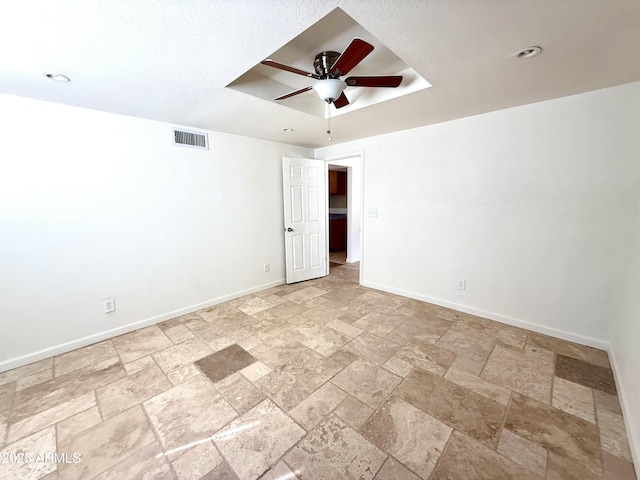 empty room with a raised ceiling, visible vents, stone finish flooring, and baseboards