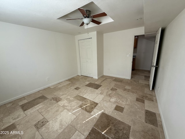 unfurnished bedroom with a closet, baseboards, ceiling fan, and stone tile floors