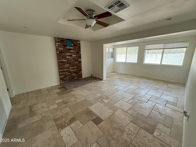 unfurnished living room featuring a tray ceiling, stone tile flooring, visible vents, a ceiling fan, and baseboards