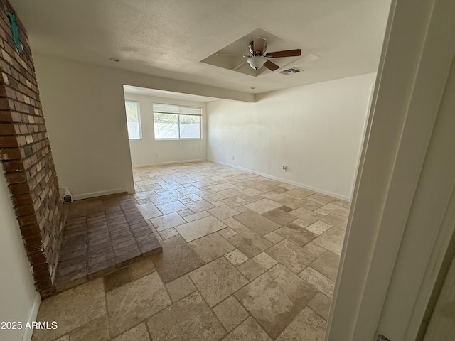 empty room with visible vents, stone tile floors, a ceiling fan, and baseboards