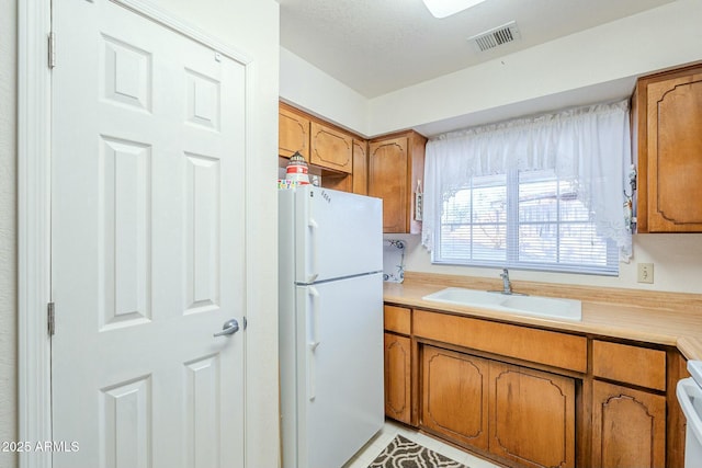 kitchen with sink, light tile patterned floors, range, and white fridge