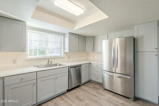 kitchen with a raised ceiling, light wood-style flooring, appliances with stainless steel finishes, light countertops, and a sink