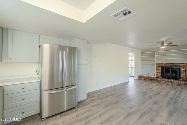 kitchen with light hardwood / wood-style floors, a brick fireplace, white cabinets, ceiling fan, and stainless steel fridge