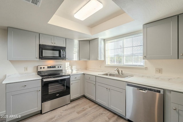 kitchen featuring stainless steel appliances, light hardwood / wood-style floors, sink, gray cabinets, and a raised ceiling