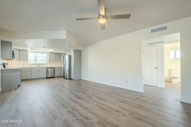 unfurnished living room with a ceiling fan, a sink, visible vents, and light wood-style floors