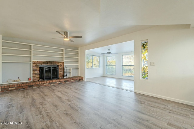 unfurnished living room with a brick fireplace, vaulted ceiling, ceiling fan, and light wood-type flooring