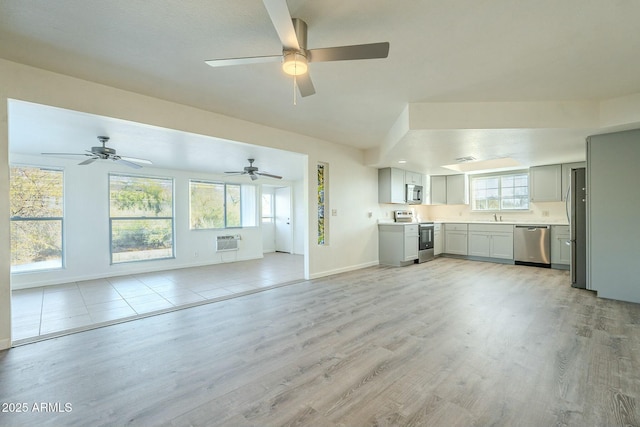 unfurnished living room featuring a sink, light wood finished floors, plenty of natural light, and an AC wall unit