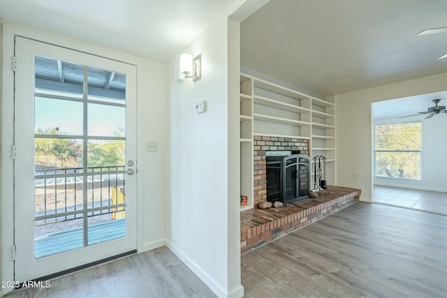 doorway to outside featuring ceiling fan, baseboards, built in features, light wood-style floors, and a brick fireplace