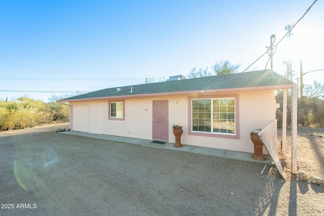 ranch-style home with a garage, roof with shingles, driveway, and stucco siding