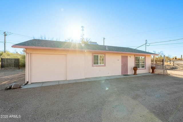 view of front of house featuring stucco siding, a shingled roof, fence, a garage, and driveway