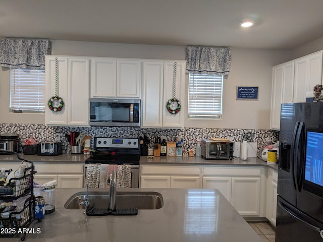 kitchen with light tile patterned floors, decorative backsplash, appliances with stainless steel finishes, white cabinetry, and a sink