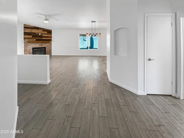 interior space with hardwood / wood-style flooring, ceiling fan with notable chandelier, a brick fireplace, and vaulted ceiling