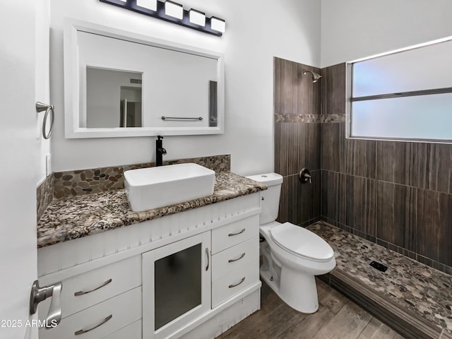 bathroom with hardwood / wood-style floors, vanity, toilet, and a tile shower