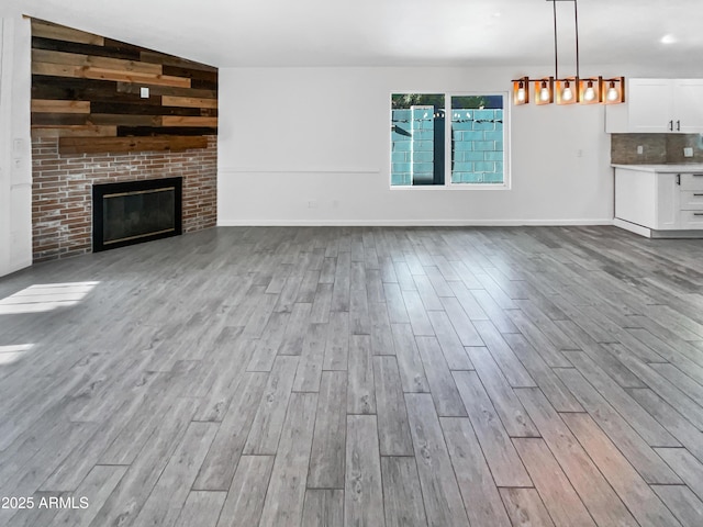 unfurnished living room with a brick fireplace, vaulted ceiling, and light wood-type flooring