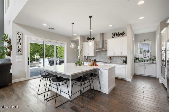 kitchen featuring dark hardwood / wood-style floors, wall chimney exhaust hood, white cabinetry, and a large island with sink