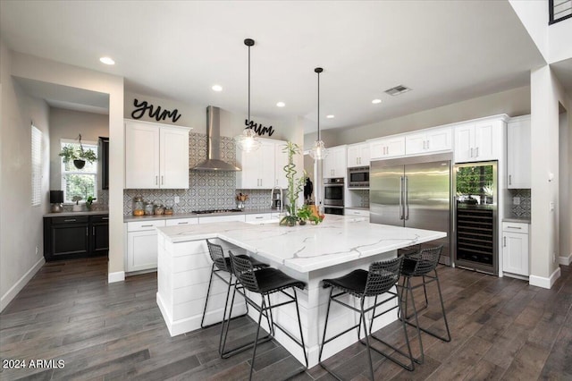 kitchen with white cabinetry, wall chimney exhaust hood, a large island with sink, and dark hardwood / wood-style flooring