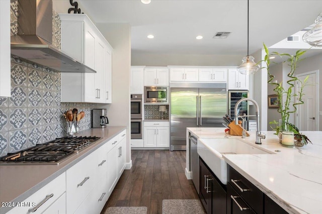 kitchen with white cabinetry, wall chimney range hood, built in appliances, dark hardwood / wood-style floors, and pendant lighting