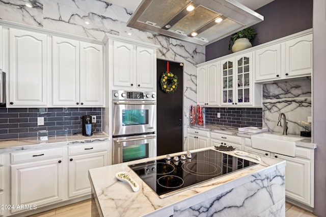 kitchen featuring black electric stovetop, stainless steel double oven, island range hood, sink, and white cabinetry