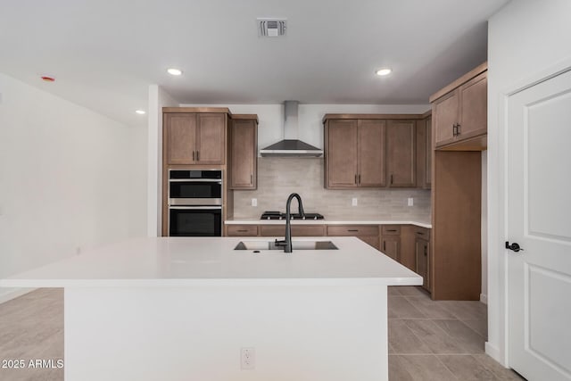 kitchen with sink, an island with sink, decorative backsplash, and wall chimney range hood