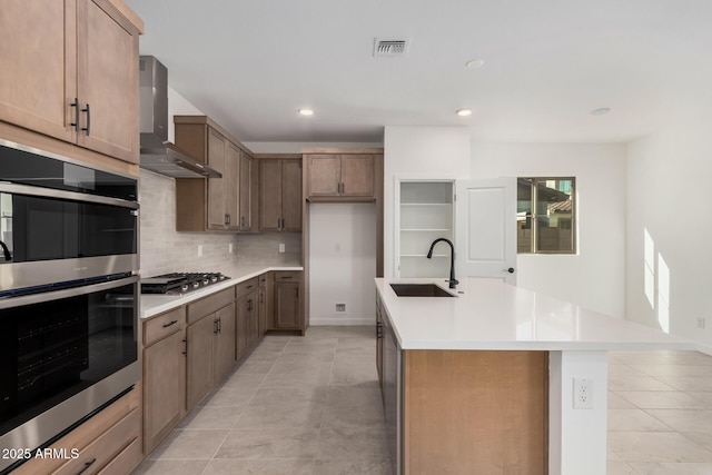 kitchen featuring appliances with stainless steel finishes, tasteful backsplash, an island with sink, sink, and wall chimney range hood