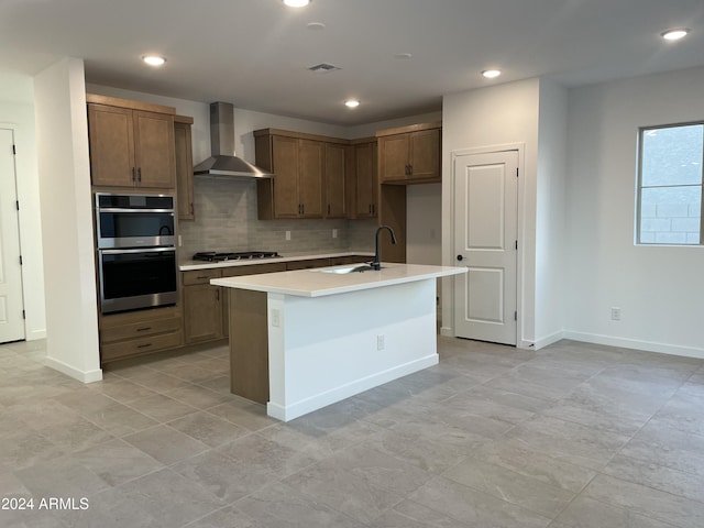 kitchen with sink, stainless steel appliances, tasteful backsplash, a center island with sink, and wall chimney exhaust hood