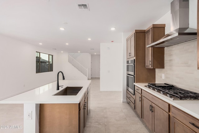 kitchen with sink, appliances with stainless steel finishes, an island with sink, light tile patterned flooring, and wall chimney exhaust hood