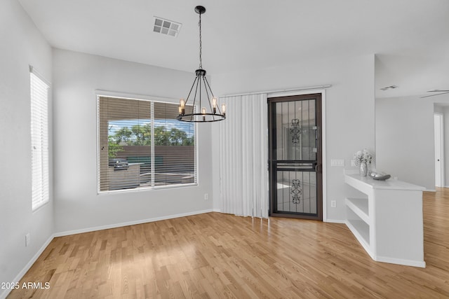 unfurnished dining area with baseboards, a notable chandelier, wood finished floors, and visible vents