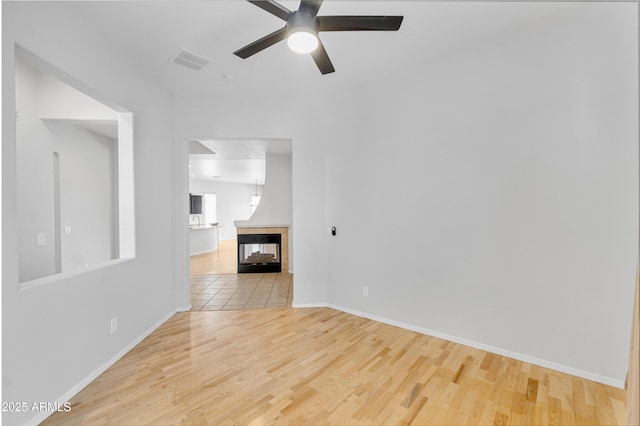 empty room featuring a multi sided fireplace, ceiling fan, wood finished floors, and visible vents