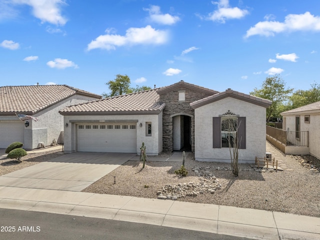 view of front of house with driveway, a tile roof, an attached garage, stone siding, and stucco siding