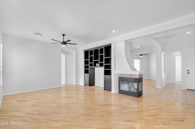 unfurnished living room featuring built in features, baseboards, ceiling fan, light wood-type flooring, and a tiled fireplace