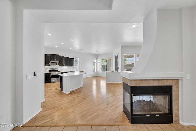 kitchen featuring open floor plan, light wood-type flooring, light countertops, dark cabinets, and stainless steel appliances