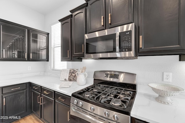 kitchen featuring appliances with stainless steel finishes, light wood finished floors, and light stone counters