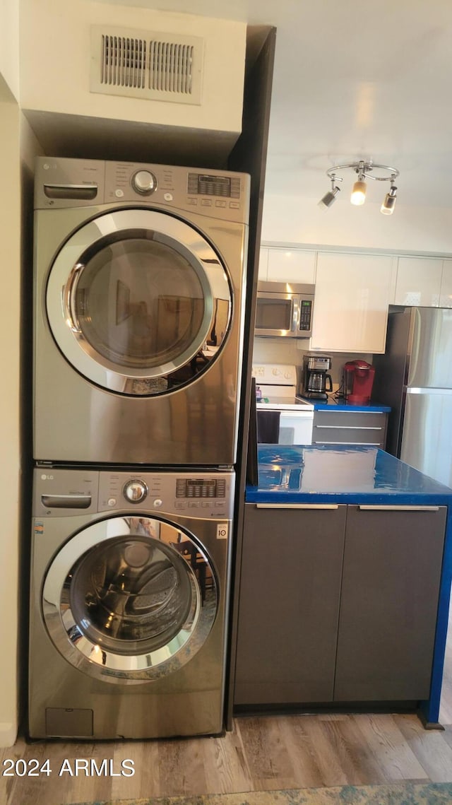 laundry area with light wood-type flooring, stacked washer and dryer, laundry area, and visible vents