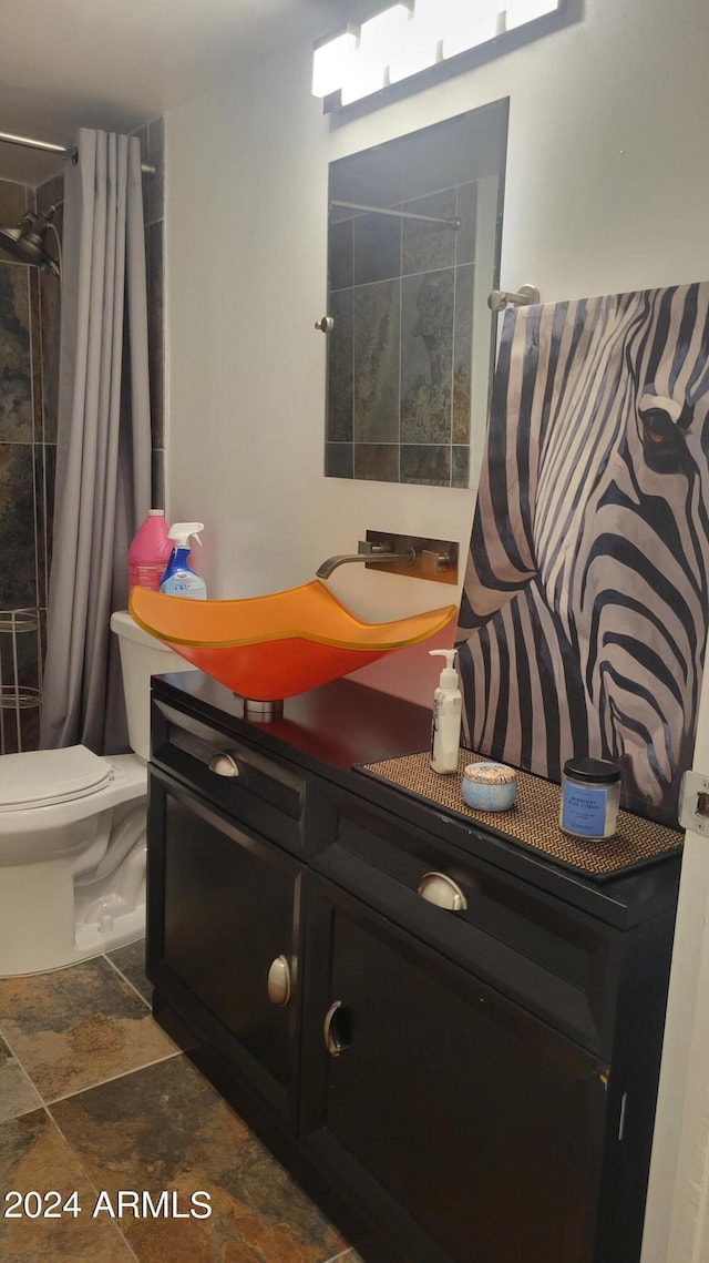 full bath with a tile shower, stone finish floor, vanity, and toilet