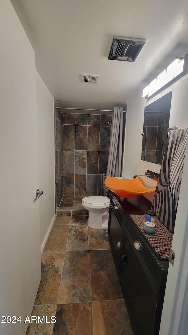 full bath featuring stone tile floors, visible vents, a tile shower, and vanity