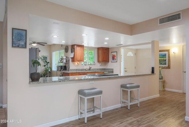 kitchen featuring kitchen peninsula, a kitchen breakfast bar, light stone counters, ceiling fan, and light hardwood / wood-style flooring