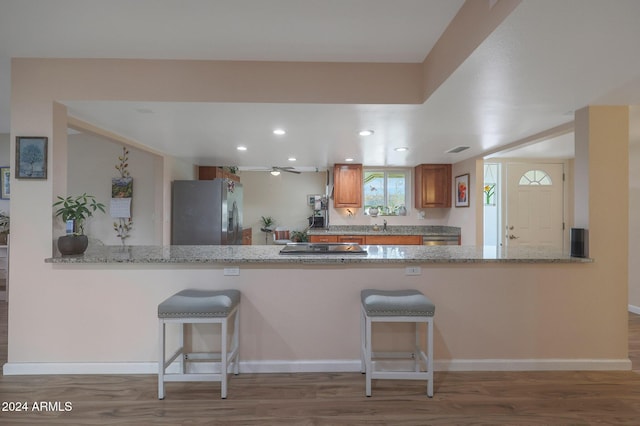 kitchen featuring kitchen peninsula, hardwood / wood-style floors, stainless steel appliances, and light stone counters