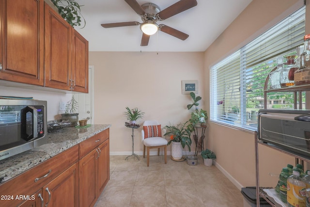 kitchen featuring ceiling fan, light tile patterned flooring, and light stone counters