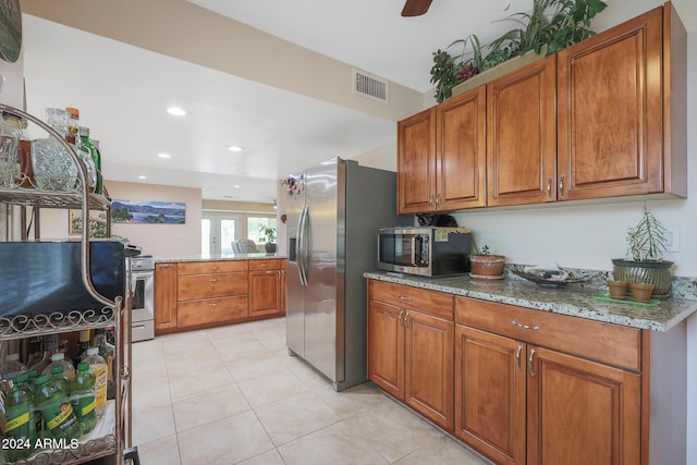 kitchen featuring light tile patterned floors, stainless steel appliances, light stone counters, and ceiling fan